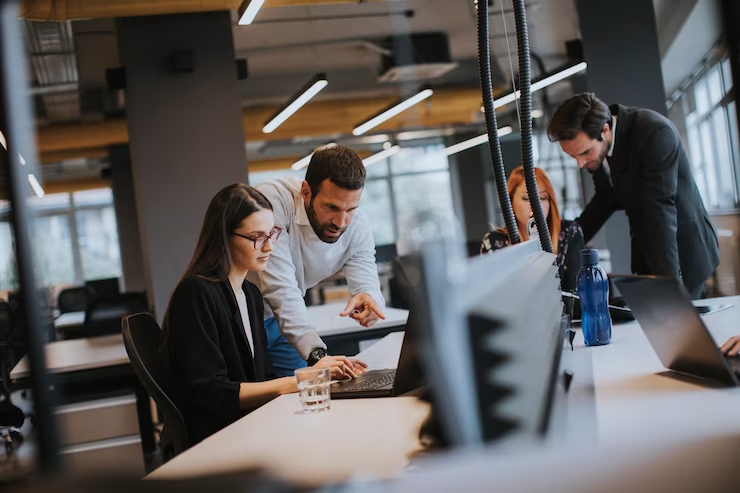 Ambiente de escritório dinâmico com uma equipe discutindo intensamente o trabalho em um laptop, transmitindo colaboração e foco em um ambiente corporativo.