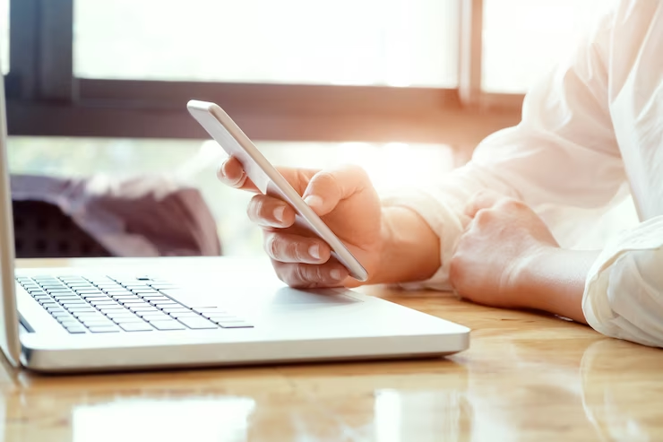 Close-up de um profissional trabalhando com smartphone e laptop, preparando-se para um clique online.