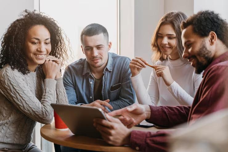 Grupo de quatro pessoas em torno de um tablet, possivelmente discutindo conteúdos que podem ser distribuídos via disparo de voz.