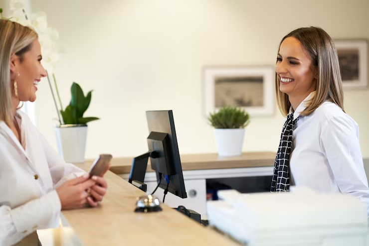 Recepção de atendimento terceirizado com funcionária sorridente usando uniforme formal com uma cliente segurando um celular.