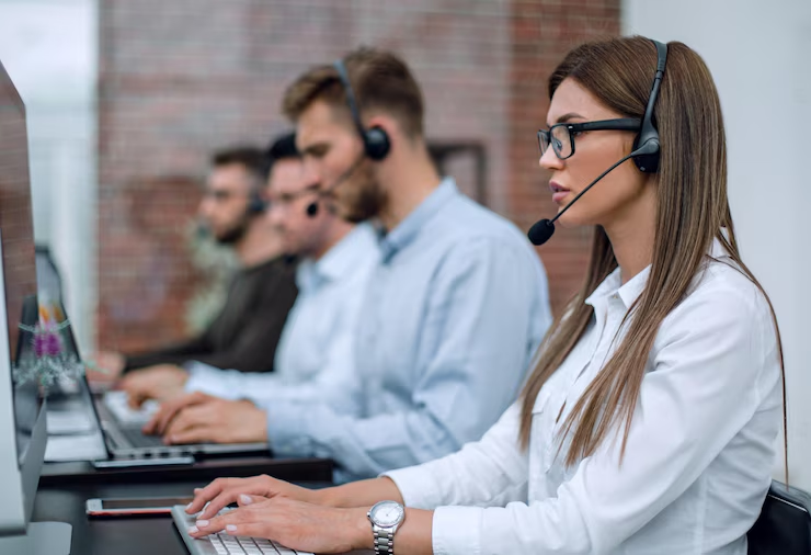 Fileira de atendentes de call center concentrados em seus computadores, usando fones de ouvido, refletindo um ambiente de trabalho dedicado a um serviço de atendimento 0800.