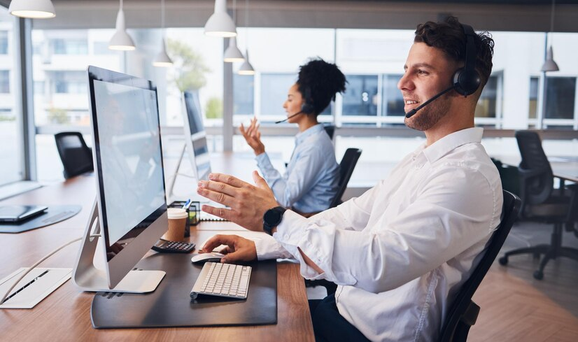 Profissionais com fones de ouvido diante de computadores em um escritório moderno, representando um ambiente de call center onde ocorrem atendimentos e assistência ao cliente.