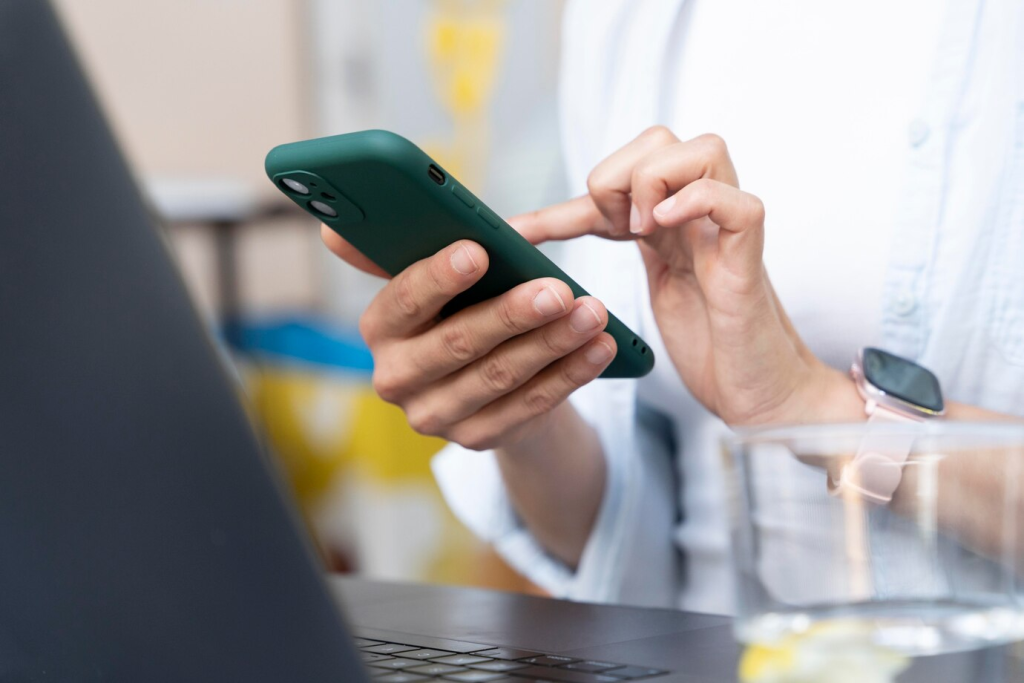 Close-up de uma mão segurando um smartphone com uma capa verde, navegando no WhatsApp, destacando o uso prático do aplicativo no dia a dia empresarial.