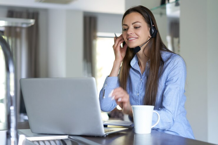 Mulher sorridente em escritório usando headset para videochamada, exemplificando atendimento ao cliente.