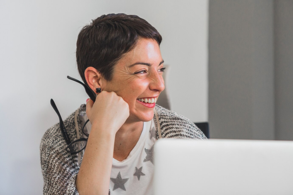 Mulher sorridente usando óculos e headset durante uma videochamada no escritório, representando atendimento ao cliente eficiente e amigável.