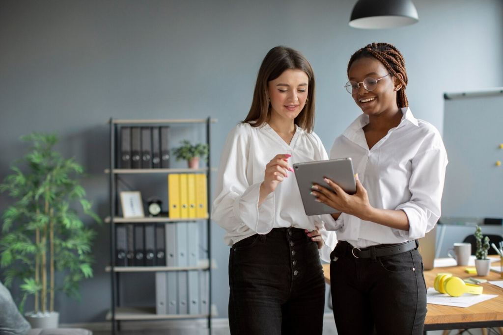 Duas profissionais discutindo estratégias em um tablet no escritório, representando a colaboração e eficiência proporcionadas pela terceirização de atendimento ao cliente.